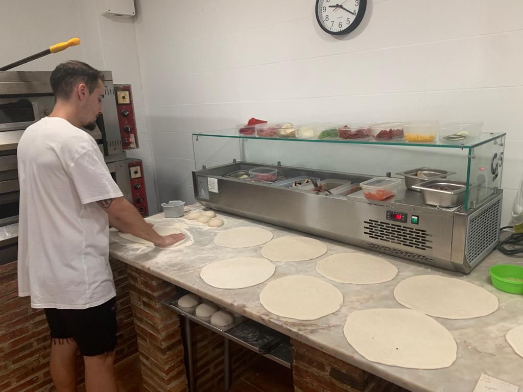 Pizzero estirando bases de masa sobre la mesa de mármol