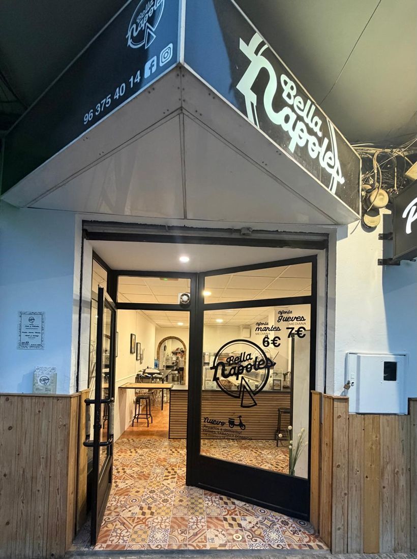 Fachada de la pizzería Bella Napoles de noche, con la puerta abierta y el suelo de azulejo hidráulico